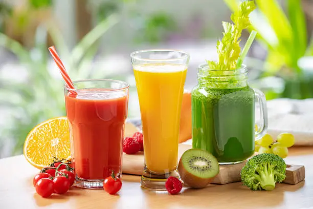 Tres vasos con diferentes jugos y zumos junto a sus respectivos ingredientes