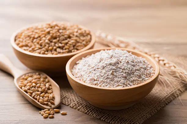 Un tazón con trigo integral y otro con harina de trigo integral