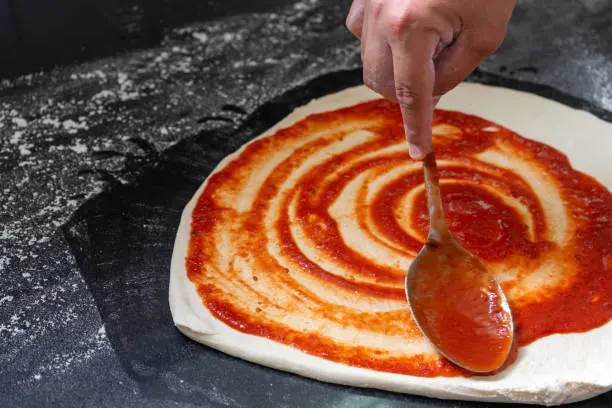 Extendiendo salsa de tomate sobre una base de pizza