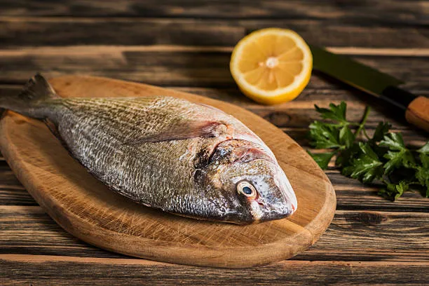 Una dorada sobre una tabla junto a un cítrico y un poco de perejil